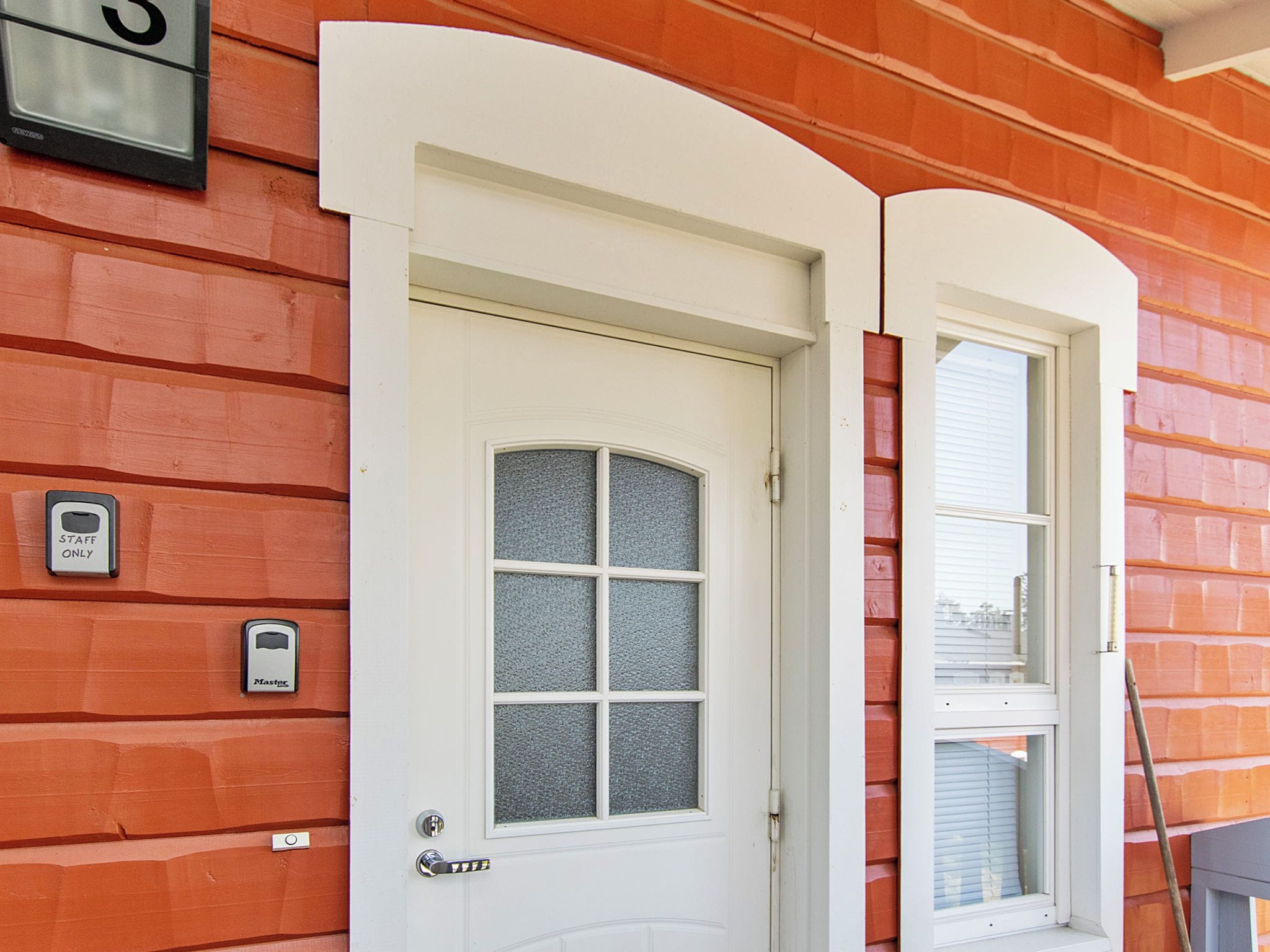 Eine weiße Tür mit Fensterglas, einer Tastatur und einem Klingelschild mit der Aufschrift 'STAFF ONLY', an einer Ziegelwand.