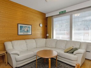 Una sala moderna con un sofá seccional color beige, una mesita redonda de madera y una fotografía enmarcada en la pared.