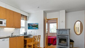 Ett kompakt bostadsutrymme med kök, matplats och en öppen spis.