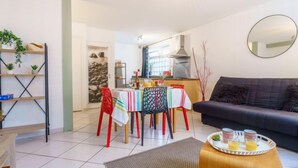 En moderne stue med en mørk sofa, et spisebord med farverige stole og et køkken i baggrunden.