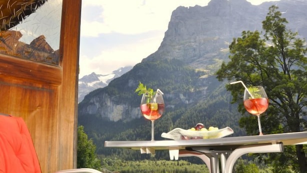 A table with two wine glasses and a plate of fruit, set against a mountainous backdrop.