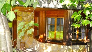 A rustic cabin with a stone exterior, a wooden window, and a stone pathway leading to the entrance.