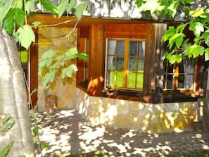A rustic cabin with a stone exterior, a wooden window, and a stone pathway leading to the entrance.