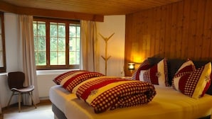 A bedroom with a large bed, wooden walls, a window with curtains, a chair, and a lamp.