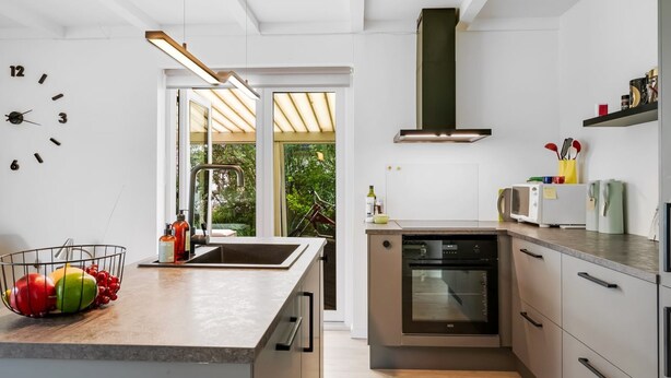 Una cocina moderna con una isla central, horno empotrado y un amplio ventanal con vistas a zonas verdes.