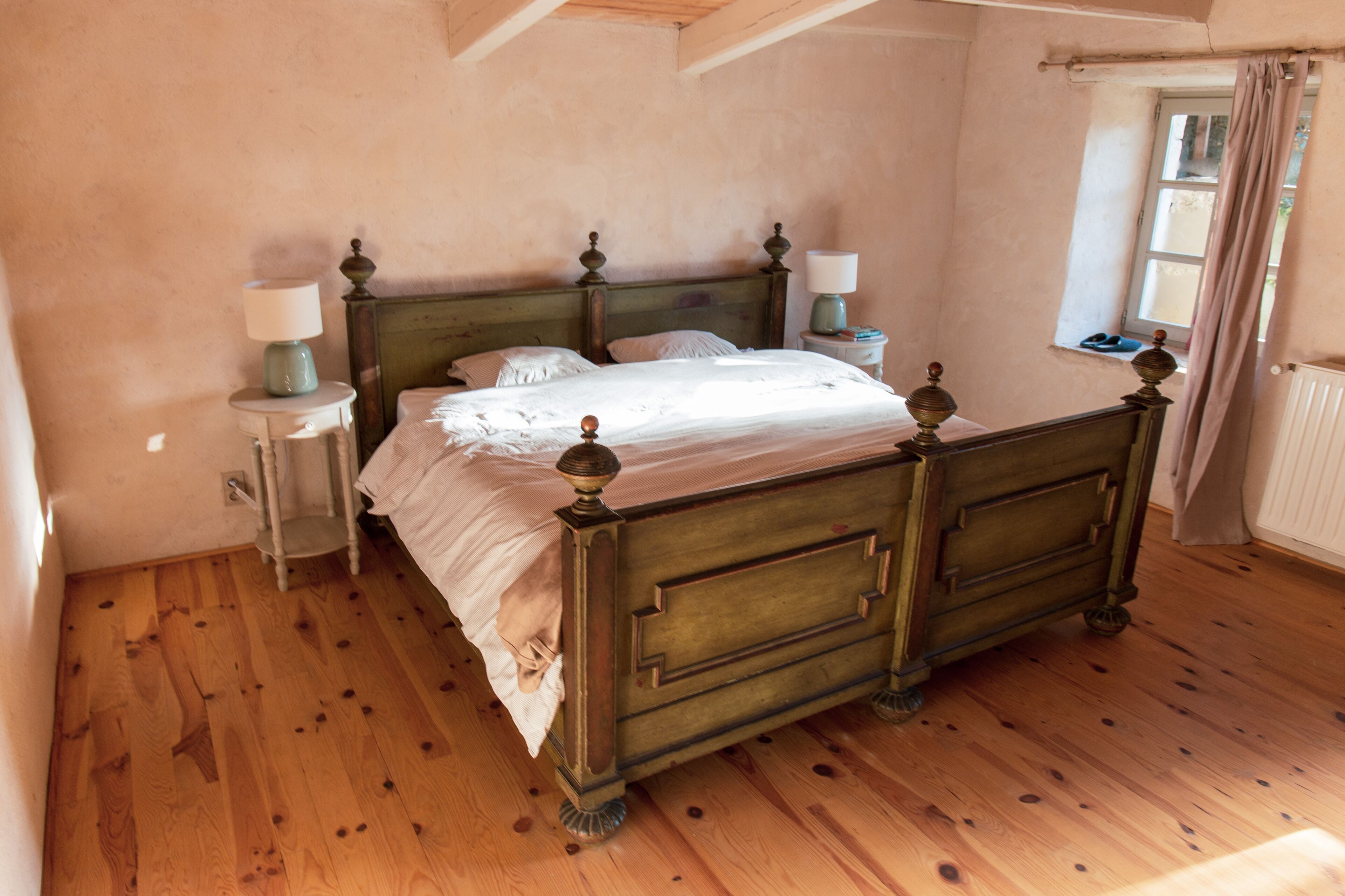 Een slaapkamer met een houten bed, twee nachtkastjes, een raam met gordijnen en een radiator.