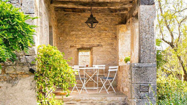 Una scala in pietra conduce a una stanza con una porta in legno, un lampadario e sedie pieghevoli bianche.