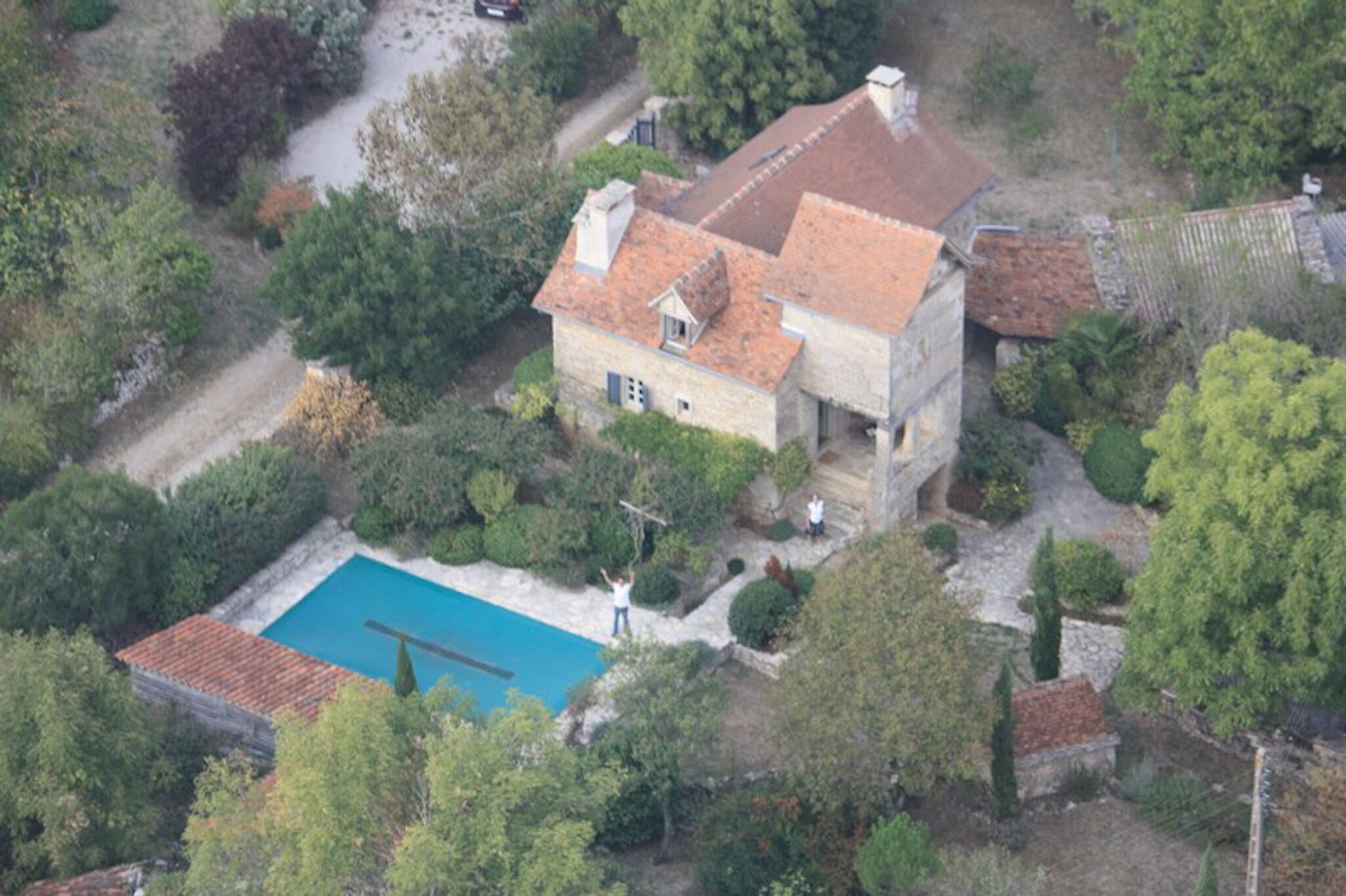 An aerial view of a house with a swimming pool, surrounded by trees and a garden.