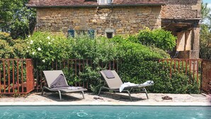 Una casa in pietra con piscina, due poltrone da relax e un recinto rosso.