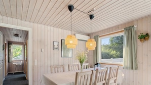 A dining area with a wooden table, chairs, and pendant lights. There is a window with curtains and a view of greenery outside. - "Viljo" - 30km from the sea by Interhome (Toftlund)