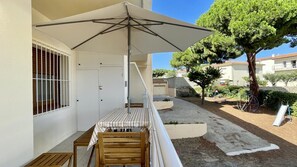A balcony with a wooden table and chairs, a striped tablecloth, and a large umbrella. - RIELLS DE MAR A1 (L'Escala)