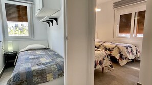 A bedroom with a single bed, a nightstand, a window with blinds, and a door leading to another room with two beds. - RIELLS DE MAR A1 (L'Escala)