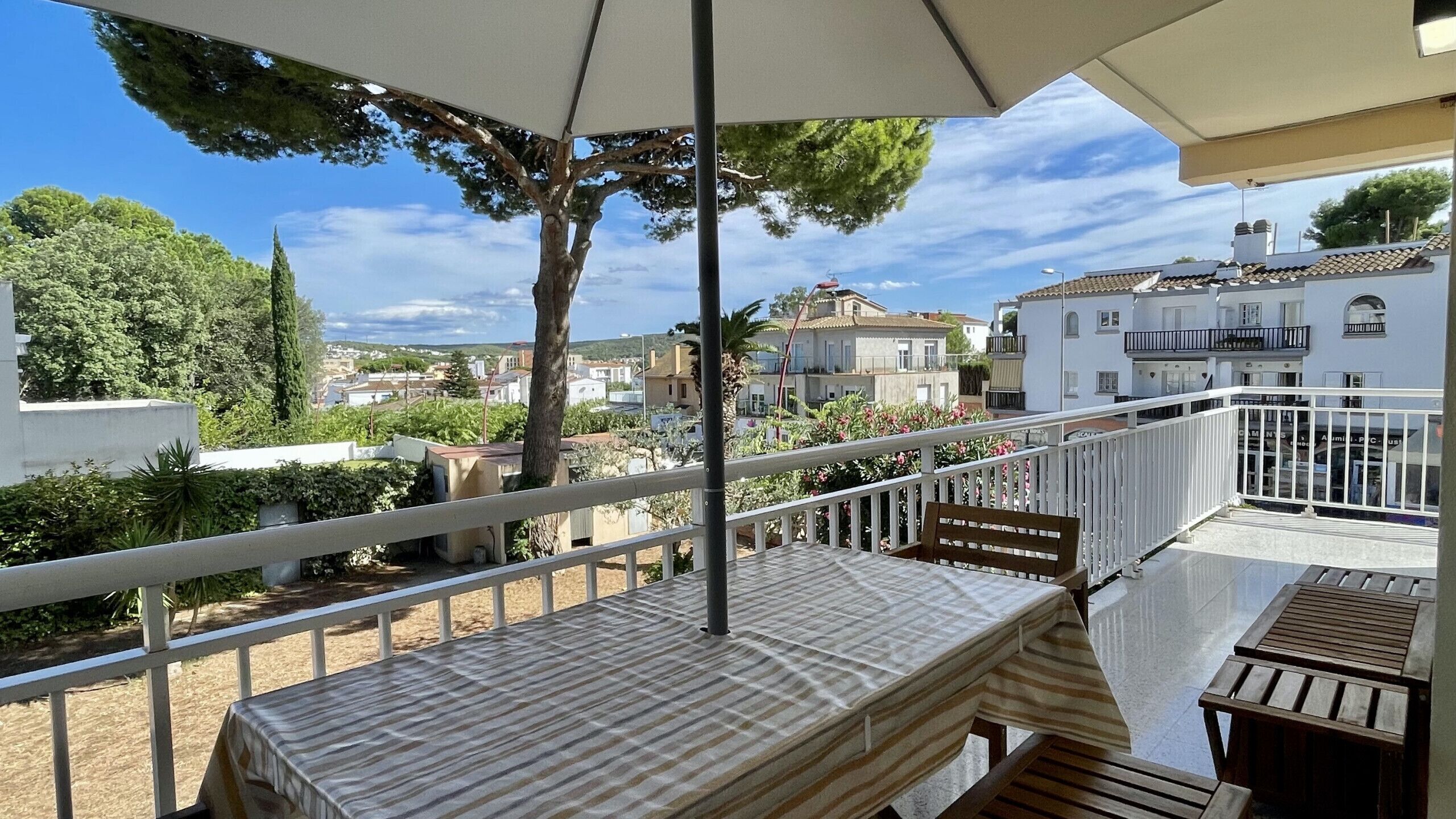 A balcony with a table and chairs, overlooking a residential area with houses and greenery.
