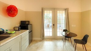 Una cocina compacta con microondas, tostadora y un adorno rojo en la pared. Hay un comedor con mesa y sillas, y una puerta que da al exterior.