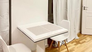 Una stanza moderna e luminosa con un tavolo bianco e due sedie bianche, pavimento in legno e porta bianca.