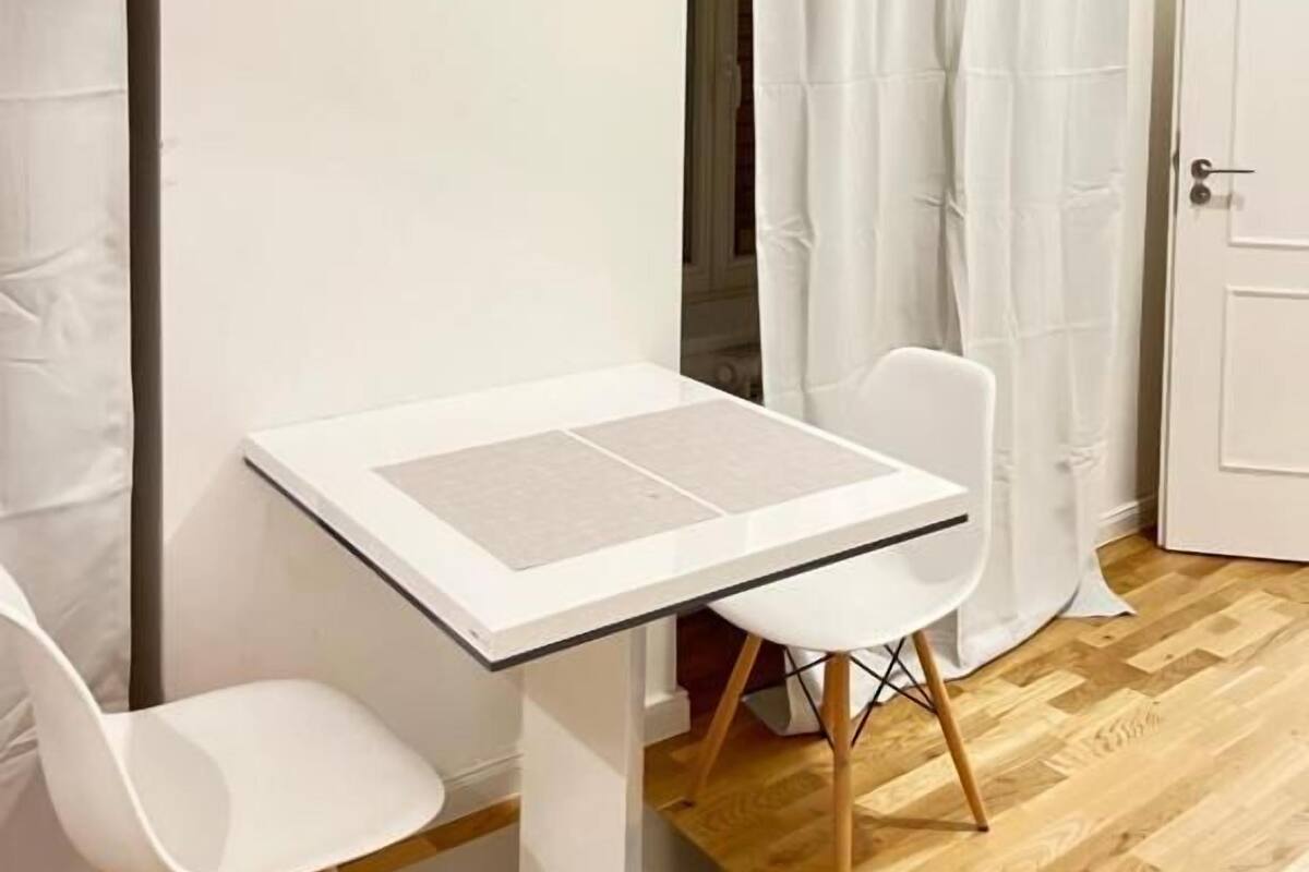 A small, modern room with a white table and two white chairs, a wooden floor, and a white door.