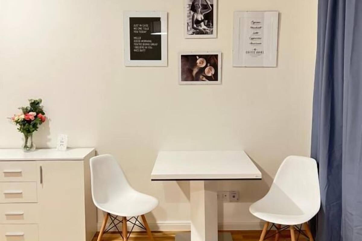 A small, modern room with a white desk, two white chairs, a wooden floor, and three framed pictures on the wall.