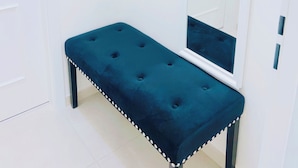 Un corridoio con una porta bianca, una panca blu e uno specchio appeso al muro.