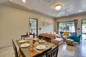 Relax in this inviting living area with a dining table, comfortable seating, and a balcony offering a view of lush surroundings.