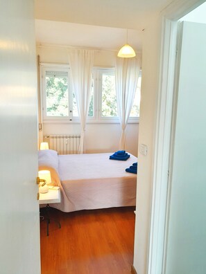 A bedroom with a bed, a bedside table with a lamp, a radiator, and a window with curtains. - Palocco Boutique (Lazio)