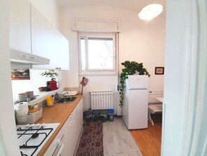 A compact kitchen with a gas stove, a white refrigerator, a window, and a radiator. - Palocco Boutique (Lazio)