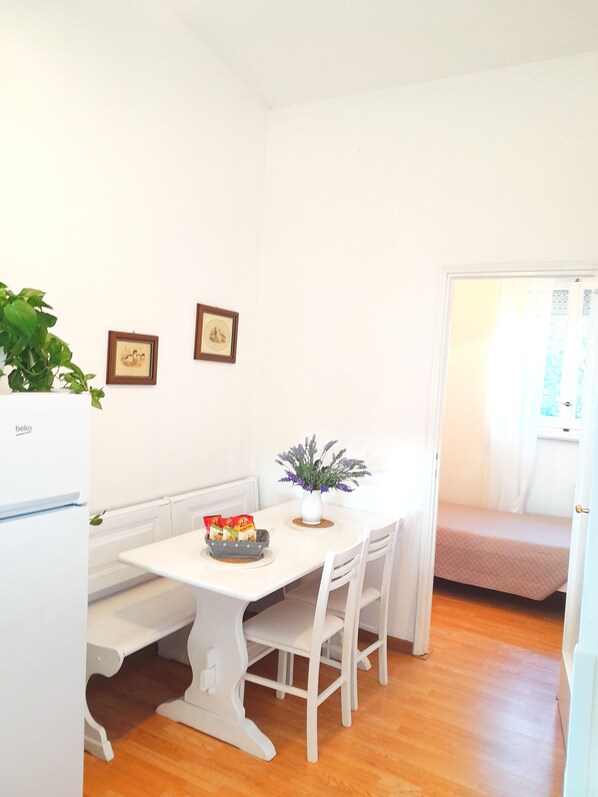 A small, bright room with a white table, white chairs, a white bench, a small plant, and a refrigerator. - Palocco Boutique (Lazio)