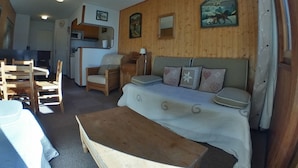 Una habitación acogedora con pared de madera, una cama, un sofá, una mesa de comedor con sillas y una zona de cocina.