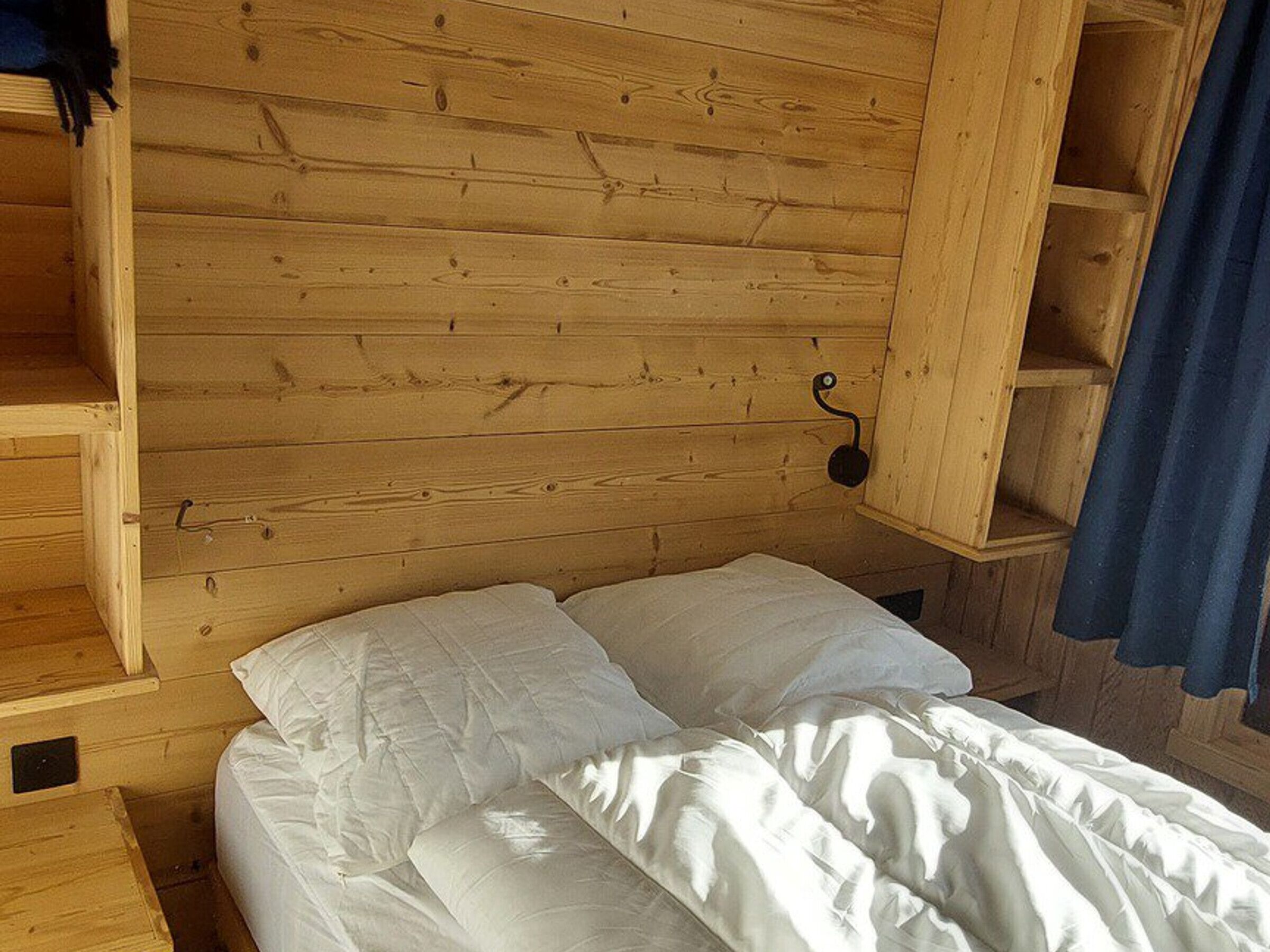 A wooden cabin room with a bed, a shelf, and a hanging light fixture.
