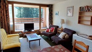 A cozy living room with a television, two sofas, a coffee table, and a bookshelf.