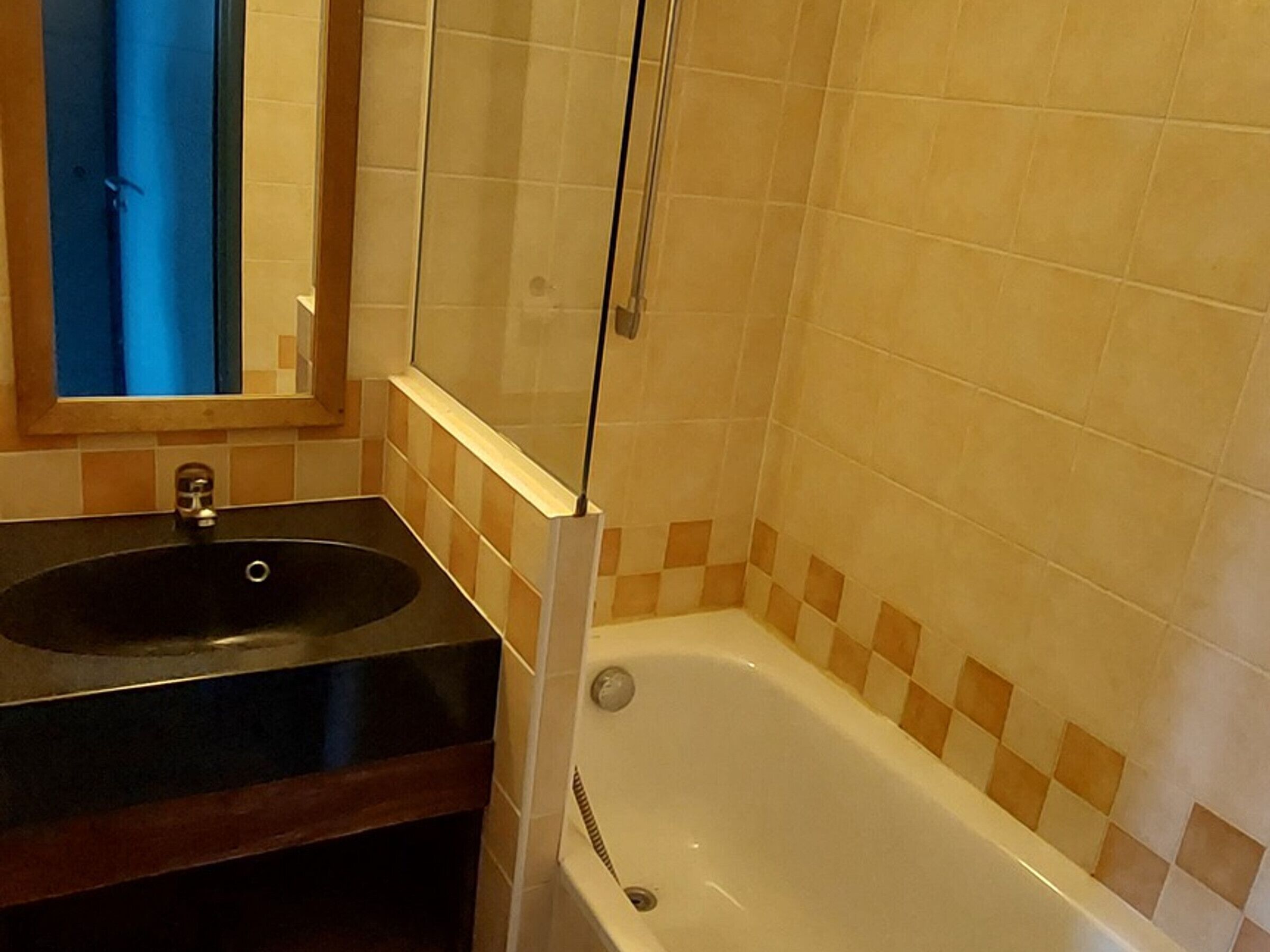 Un baño con un lavamanos negro, un espejo y una bañera blanca con baldosas de cuadros.