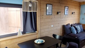 A cozy room with a wooden wall, a black table with a bowl of decorative items, a black sofa with cushions, and a hanging light fixture.