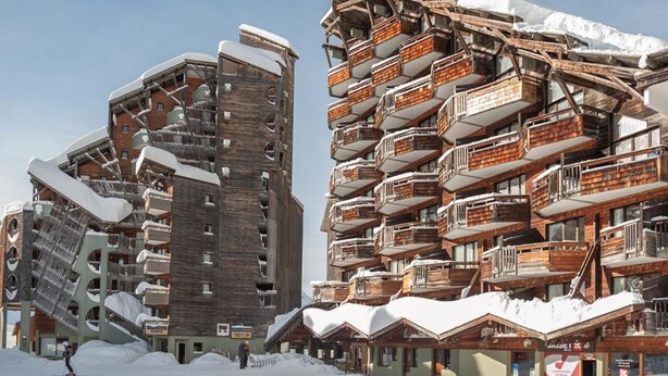 A snow-covered ski resort with unique wooden buildings featuring balconies and ski lifts.
