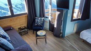 A cozy room with a bed, a chair with a cushion, a small table, and a TV.
