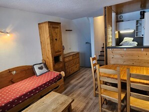 Quarto compacto com cama, banco, cômoda e mesa de jantar de madeira, todos com cadeiras.