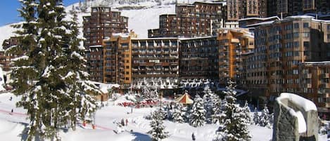 Une station de ski enneigée, avec des bâtiments à plusieurs étages, des pistes de ski et des arbres recouverts de neige.