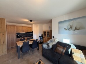 Eine moderne Küche mit Holzschränken, einem Esstisch mit Stühlen und einem schwarzen Sofa mit Felldecke.