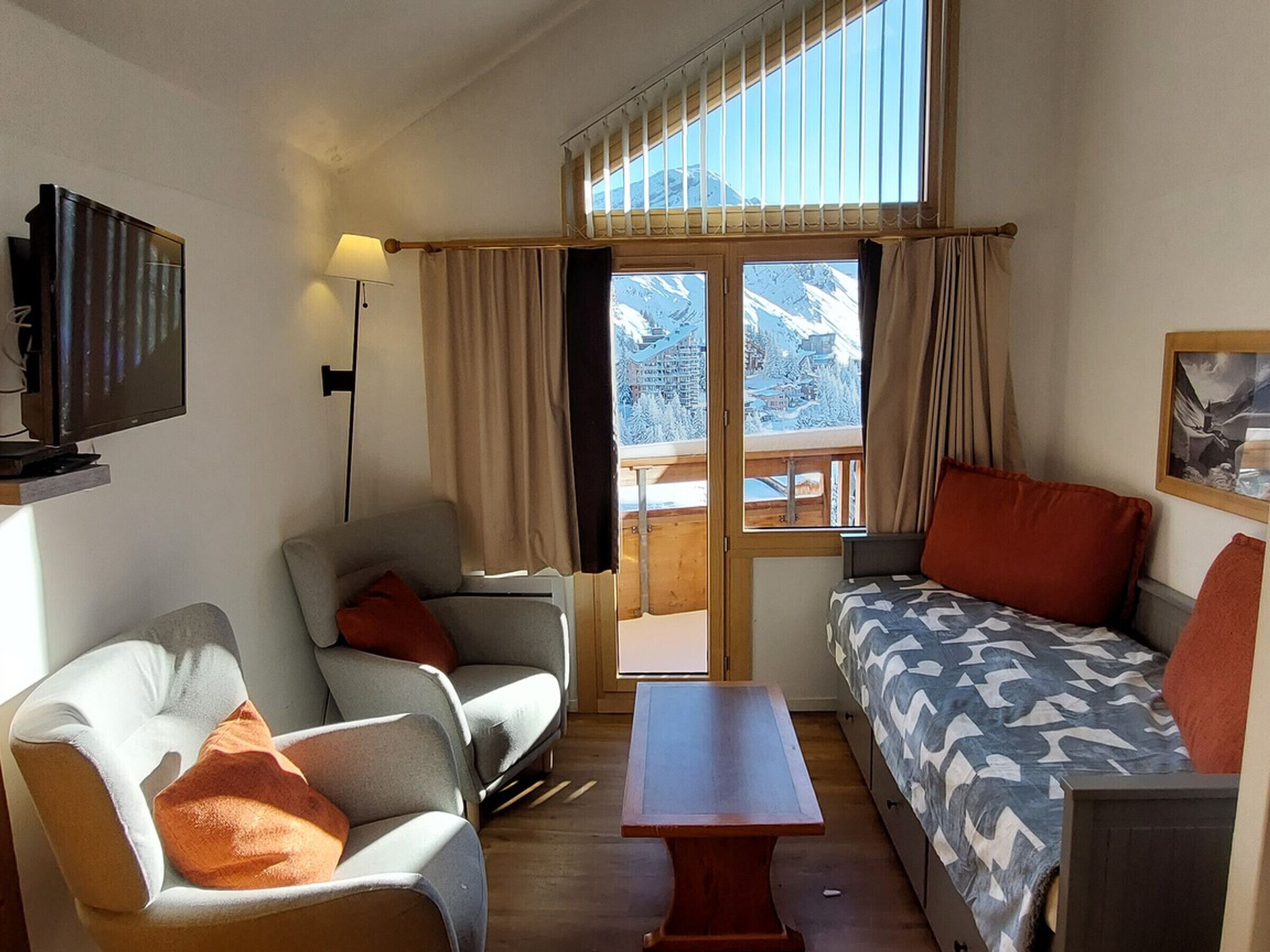 Ett mysigt rum med en soffa, två fåtöljer, ett litet bord, en tv och ett fönster med utsikt över snötäckta berg.