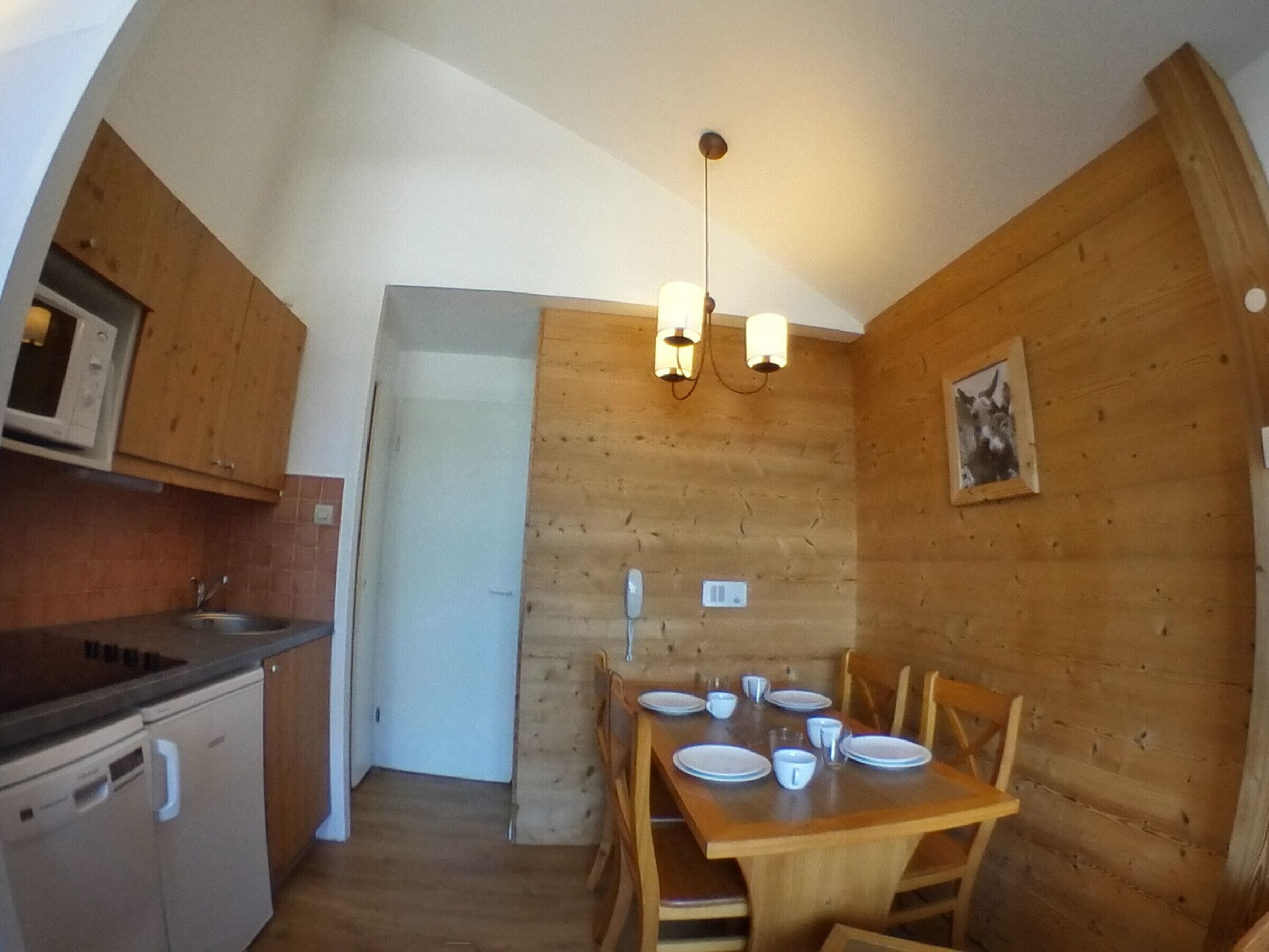 Una cucina compatta con mobili in legno, un forno a microonde integrato e un'area pranzo con tavolo imbandito per quattro persone.
