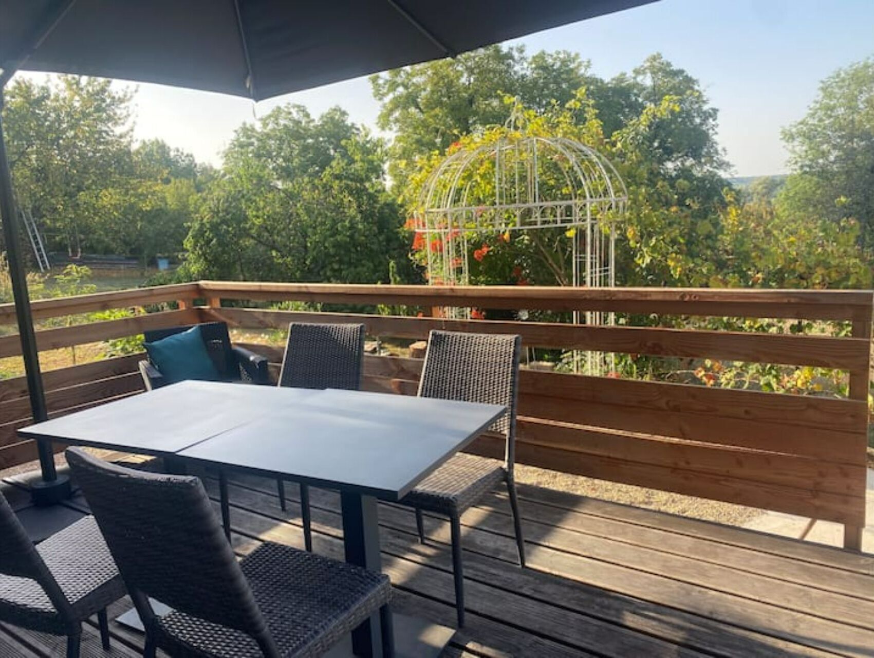 An outdoor patio with a table and chairs, a wooden deck, and a metal birdcage with flowers.