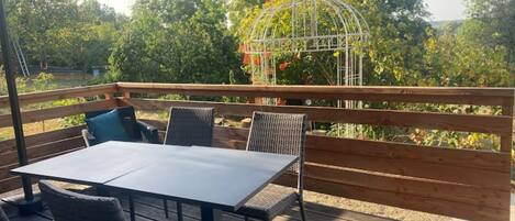 An outdoor patio with a table and chairs, a wooden deck, and a metal birdcage with flowers.