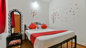 A bedroom with a bed, a mirror, a nightstand, and a red chair. - Route 77 (Calangute)