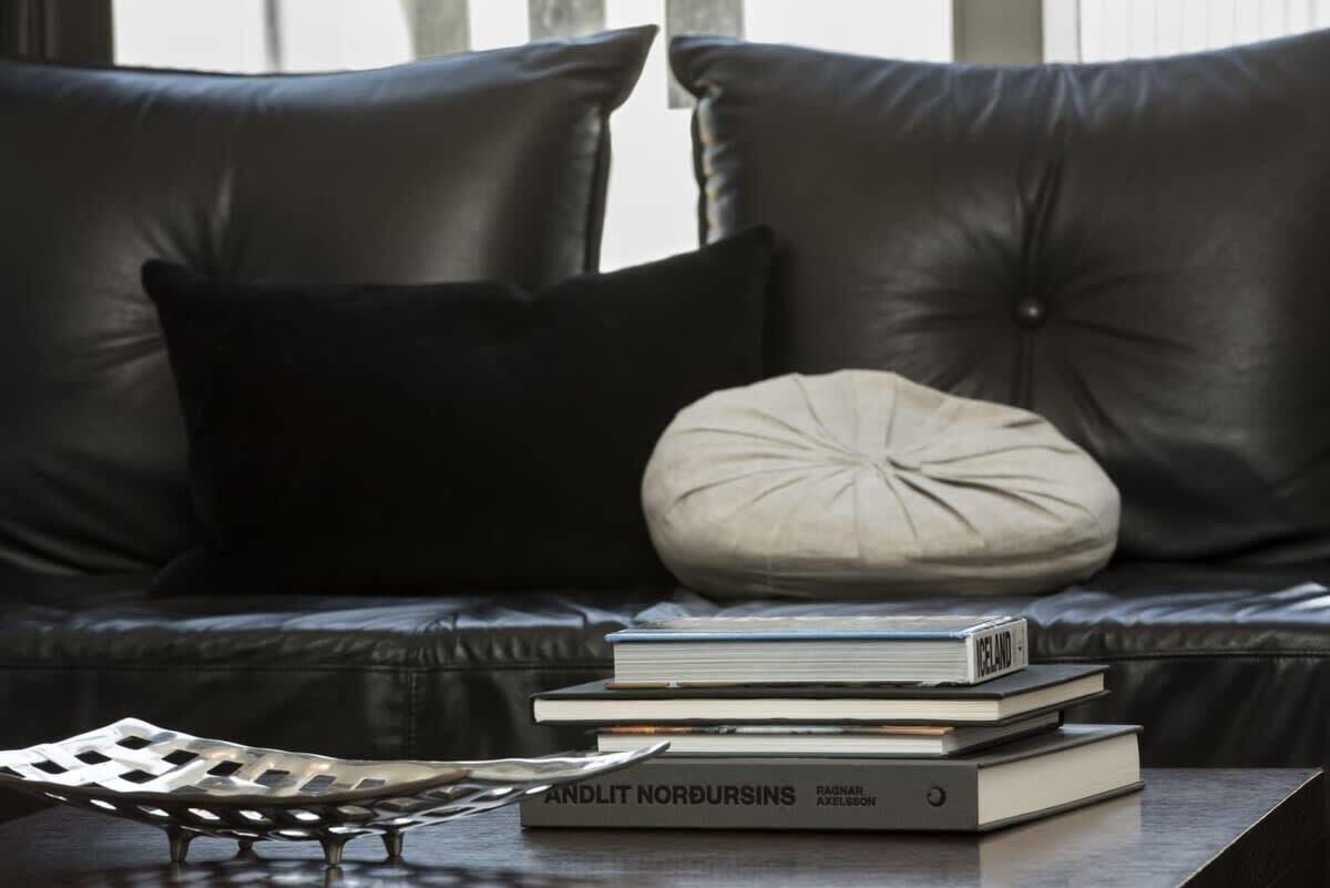 Un sofá de cuero negro con un cojín blanco y una pila de libros sobre una mesa.
