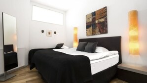 A modern bedroom with a large bed, a bedside table, a mirror, and a wall-mounted artwork.