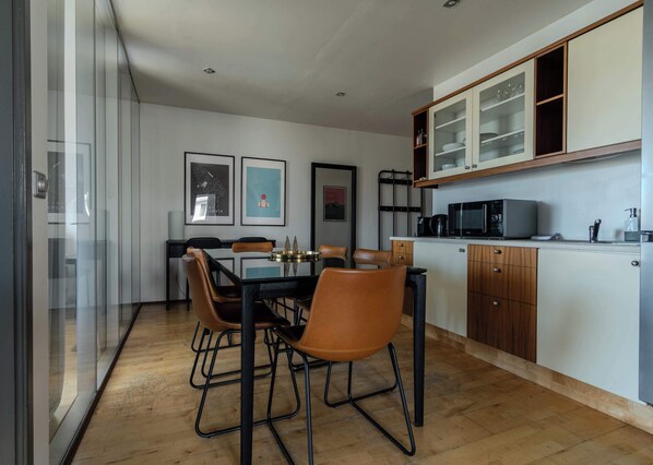 Una cocina moderna con comedor, que incluye una mesa de vidrio, sillas de madera y un microondas.