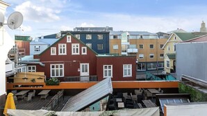 Un edificio de varios pisos con fachada roja y ventanas blancas, que cuenta con asientos al aire libre y una antena parabólica.