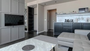 A modern living room with a flat-screen TV, a sofa, a coffee table, and a kitchen area with a microwave and cabinets.