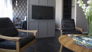 A modern living room with a flat-screen TV, two leather chairs, a wooden coffee table, and a bookshelf. - Mani Apartments -Studio with Balcony Downtown (Reykjavík)