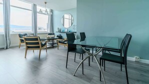 A modern dining area with a glass table and chairs, a round mirror, and a view of the city through large windows.