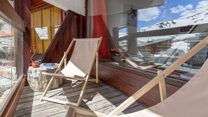 Une terrasse en bois avec une chaise et une table en bois, une fenêtre donnant sur des montagnes enneigées et une lampe.