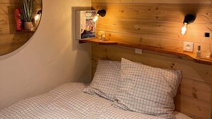 Une chambre confortable avec une tête de lit en bois, un miroir rond et deux lampes de lecture fixées au mur.